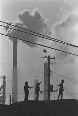 凧揚げをして遊ぶ子供たちの向こうに、煙を吐き続ける煙突